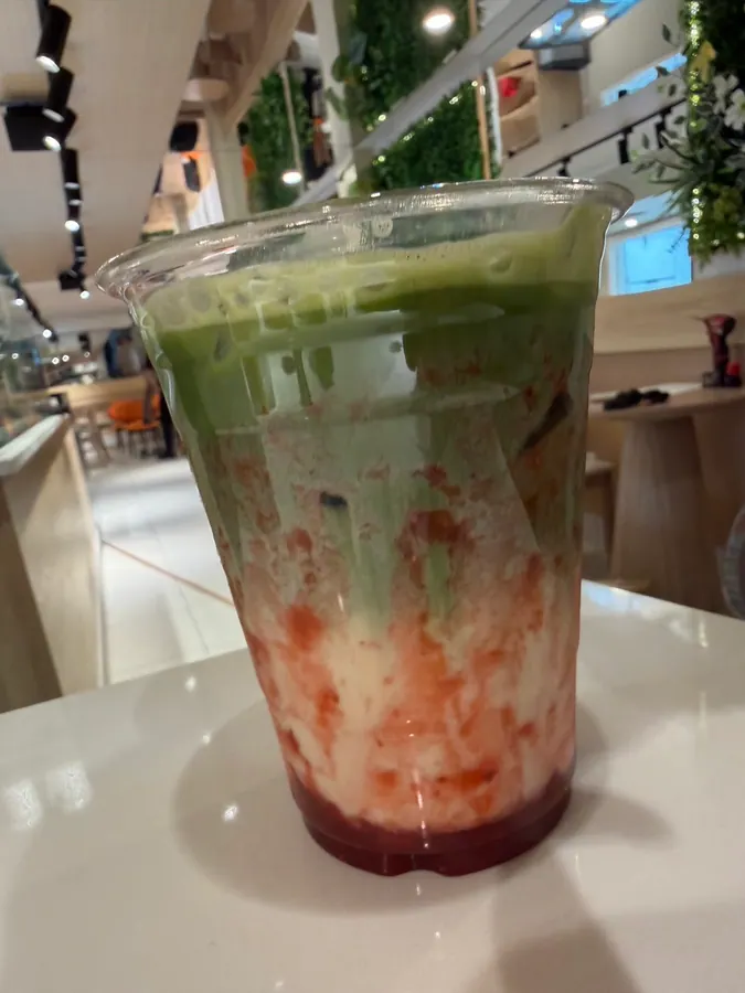 Iced strawberry matcha latte with cafe living wall in the background